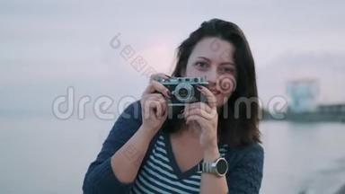 一个带复古相机的女孩的肖像。 年轻女子在海边的老式照相机上拍照